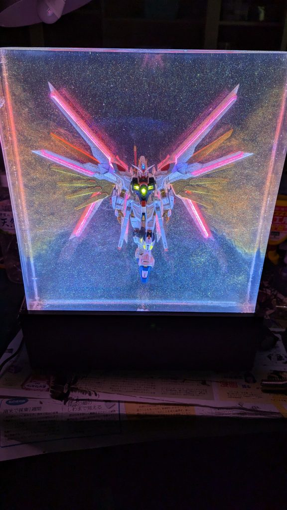 表面の研磨を行って、専用の自作枠を取り付け暗所で光らせた図。これが完成形となります。ランダムサンダーとかいう高価なものがまたうちにはなかったので表面の研磨は手作業で行っています。そのため若干透明度が落ちています。台座・枠は自作しました。スイッチ、DCジャックが付いています。下から照らしてるLEDはダイソーの2mテープLEDです。総括基本的な工作に加え電飾、レジンアートとかなり盛り沢山、オールスターなものを作れました。いい経験にはなったと思います。しかしながらこのレジン13,000円もするんですよ4kgで。この作品それを12kg使っていてしかも1層分約1kgが事故により無駄になっています。それによって設備投資込みで総額6万円程度この作品に費やすことになってんですよ。確かに出来上がった作品はいいと思えるものですがあまりにも費用がかかりすぎています。もう2度とやりたくない、そう感じさせてくれる作品でした！