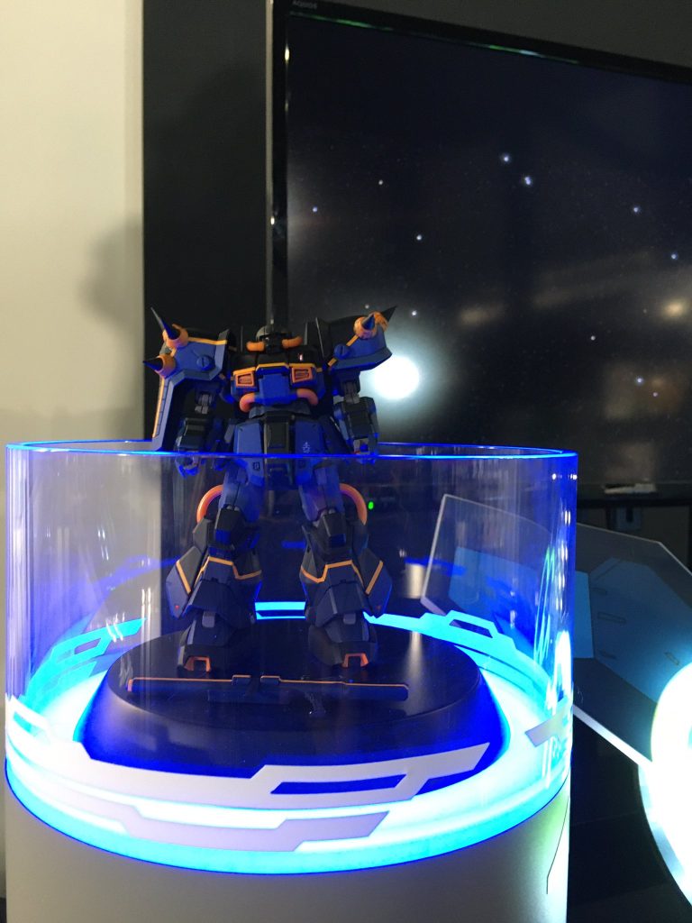 説明が終わり次第ゴーグル装着。僕もそうなんですが、メガネ着用の方はメガネのままゴーグル装着可能かいったん内径に合わせてフィッティングを確認、内径に収まればそのままゴーグルを装着、ピント位置を調整して固定してもらいます。 装着後は正面にあるスキャンデータ見る用の小型のコントローラを手にいざVRルームへ!「ビルドダイバーズ」のGBNに入るシーンを彷彿とさせる映像とシートの微細な振動、正面から吹く風を味わうことができます。VRルーム内ではスキャンデータが取り込まれるまでの間に30秒間隔?で視点が切り替わりますが特に移動はできず…ここはちょっと歩き回れるようになった方がより楽しいかなと思います。 そしてお待ちかねのスキャンデータを手元でぐるぐる回して見た時は「あれ?そこ(お立ち台)にあるのに、あれ???」となるくらい精巧に再現されてて感動しました!<3:バトルスタート!> ぐるぐる回して自分のハイザック・カスタムの3Dデータに舌鼓を打ったらいざバトル!...の前に格納庫に入り、自機を見上げます。 ハイザック・カスタムを見上げた瞬間「お、俺今アスワン(※T3部隊の艦)にいる〜〜〜!!!」と声に出てしまうくらい感動しました………。あの時の僕はもうカール・マツバラになりきってました。エリアルドやマーフィー隊長、オードリーとかヘンドリクスさんとか絶対同じ空間にいたもん。 そしていざ発進、チュートリアル後にバトルパート。チュートリアルはレバー操作の慣らし。隕石を回避、あるいは破壊しつつ仮想敵のザクともちょっと交戦します。この時、左右レバーでの操作でどの方向に移動できるかの説明が出てきます。左右にレバーを倒すと左右に平行移動するのは共通で、左レバーは残後に倒すと上下、右レバーは前後に倒すと前後移動、だったかなと思います。逆だったかもしれねェ.... バトルはネオ・ジオング戦!腹部、指のメガ粒子砲を撃ってくるので避けつつ攻撃。武器はエネルギー切れなどないですし、気にせずやたらめったら撃ってOKでした。