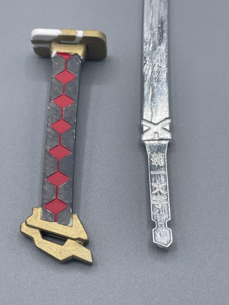 ガーベラストレート（和訳で菊一文字）　刃部分にはメッキ処理が施され、波紋まであるこだわりの造形。しかも、ガーベラストレートの名前の由来である「菊一文字」の銘まで打たれているいるという衝撃。豆知識！？　今となっては、レッドフレームの代名詞とも言えるガーベラストレート。しかし、その設定が出来上がる前に発売された、コレクションシリーズやＢＢ戦士版のキットには、このガーベラストレートが付属しませんでした。そのため、今の目で見ると少し物足りなく感じてしまうキットになっています。  過去作とはいえ、アップにすると塗装の雑さが目立ちますねぇ^^;