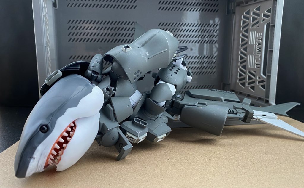 〜♪〜♪(MSイグルーの例の曲)　光。目も眩むような光。ほんの数時間前まで宇宙(そら)という暗闇にいた僕達には眩し過ぎる光だ。　僕は、オリヴァー･マイ。ジオン公国軍第603技術試験隊技術中尉だ。僕達は今、地球。ジオン勢力下の海沿いにある、主に水中用MAを運用する部隊の補給を担う基地にいる。この基地は、その立地条件から水陸両用MSなどのテスト運用などにも使用されている基地だ。そう、僕達はあるMSの運用試験の為、ここにいる。　実をいうと、この基地には二度目、…だったりするのだが。前回、僕達はここであるMSの試験に立ち会った。XMSM-03S シャークゴッグ。ツィマット社、そしてASLM社の二社合作による機体だ。…その外見は、名は体を表す。というか…。まあ、それはいい。そうして今回、僕達、いや、「我々」第603技術試験隊に、正式採用された(されてしまった？)MSM-03Sシャークゴッグの最終試験が依頼されたのだ。　暑い夏の日差しをその身に受け、僕は基地と、海に面して大きく口をあけるハンガーの間にあるビーチ脇の小道を歩く。砂を踏む「サンダル」越しの感覚が心地良い。海からの風を受け、着ている「パーカー」の前を開け、首に掛けたタオルで汗を拭う。そうしてビーチ沿いを歩く僕の背に声をかける人物がいる。「ほお〜、オリヴァー･マイ技術中尉。随分と涼しげな格好をしているな。どうやら、技術中尉殿はこの任務の重要性をお分かりになっていないようで」　モニク･キャディラック特務大尉だ。その声のトーンに何かただならぬ気配を感じ、慌てて振り向く僕の目に飛び込んできた光景。それは、ピシリと「軍服」を着た、第603技術試験隊。「みんな」の姿。　何も言えず固まっている僕に、特務大尉の怒号がとぶ。「オリヴァー･マイ技術中尉っ！貴様何を腑抜けているかっ！」　人差し指をビシリと突きつけ叫ぶ特務大尉。そんな彼女を諌めるように、マルティン･プロホノウ艦長は言う。「まあまあ、キャディラック特務大尉。…特務大尉の言いたいこともわかるが。この気候、この暑さだ。ストレスを感じずに任務を遂行する為と思えば、その姿もまた、むべなるかな」　…艦長、それフォローになってません。…って、待ってくれ、前回の任務の時は僕だけが軍服だった。それなのに、何故。僕だけが…。