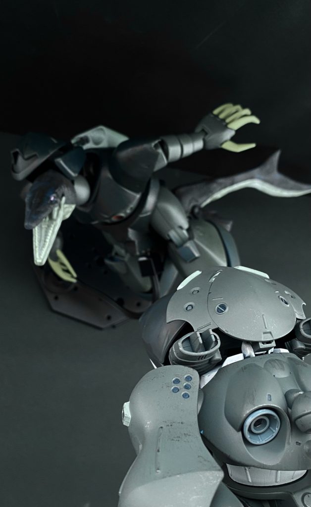 「…っ！前方っ、MS反応っ！」　モニターを見る者達に緊張が走る。…一体どこから。先程からソナーにはワシヤ機しか映し出されていない。「ワシヤ中尉っ！別の何かと見間違いの可能性は？」「そんなことないっ、…あれは確かにMSだったっ！…こちらのパッシブソナーには反応なしっ。アクティブソナーっ…」「待ってくださいっ、中尉。相手がなんであれまだこちらに気付いていない可能性もありますっ！」　しかし、僕の声が届く間もなくモニター、シャークゴッグのメインカメラからの映像を映し出すモニターに、我々は信じがたいものを見る。「ぬうぅ、あれは一体…」「…な、なんて、ナンセンスな」　後ろで騒ぐ特務大尉らをよそに、モニターの向こうの中尉に的確に指示を出す。いや、出来ない。…なんだアレは！「ちょっ！襲ってきたんですけどっ！」　半ばパニックになっている中尉に対して、落ち着いてください。と声をかけるものの、自分でも今、目にしているものが理解出来ない。…あれは、ゴッグ？…我が軍の、あの機体がなぜ？…それより、あの頭部？はなんだ。それに、尻尾がある…？　自分も、現場にいるワシヤ中尉も理解が追いついていかないまま、戦闘に入る。海中戦に特化した機体構成のシャークゴッグではあるものの、相手のゴッグ？もまた、水中での機動性は高い。