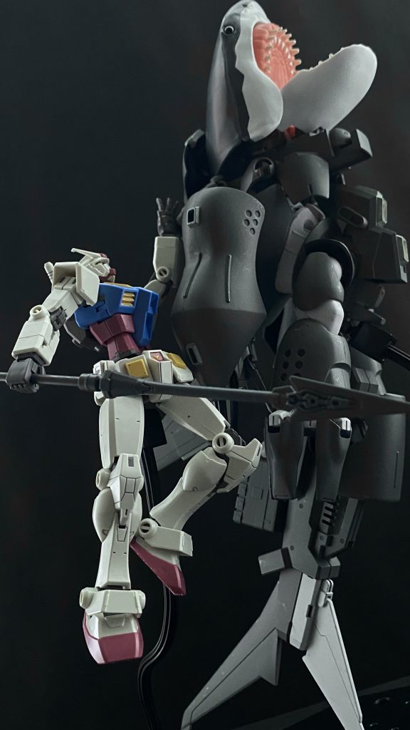 「絶対にプラントに傷を付けるな！」　乱立する油田プラントの足を避けてゴッグ？に攻撃するものの、水中を自由に動き回るゴッグ？に翻弄される。「水中じゃ、ワニ頭の方が上か。…そうか、「上」か。サメ野郎っ、俺をプラントの上まで連れて行け！」「ど、どうやって…？」「ジャンプだ。俺を背に乗せて海上にジャンプしろ！後はガンダムの推力で飛べるっ！」　機体に微かな衝撃、見るとシャークゴッグの背に装着された推進ユニットにガンダムが取り付くのが見える。…しかも、サムズアップまでしている。「…その後は、ワニ頭を下から追い立てろ、ヤツを海面上に出してやれっ！」　そうか。水中であれだけ動けても、空中じゃそうはいかない。「よしっ！…掴まってろよっ！」　思わず声を張り上げてしまう。スロットルを上げ、フットペダルを踏み込む。ガンダムをその背に乗せたシャークゴッグは、その巨体を海面に向け、ぐんぐんと上昇させる。　海面に近づくにつれ明るくなっていくメインモニターを見ながら無意識のうちに叫んでしまう。「「いけっー！」」　二人の声が重なる。どうやらガンダムのパイロットも同じだったようだ。　激しい衝撃と共に激しい光がコクピット内を照らす。太陽の光だ。モニターの中ではガンダムが大空に飛翔するのが見える。その機体が見る間に小さくなる中、二度目の衝撃がシャークゴッグを襲う。着水したのだ。再び闇に覆われるモニターを見ながら、先ほどの言葉を思い出し、ゴッグ？の姿を探すとフットペダルを踏み込む。…後はあのゴッグ？を海面上に追い立てるだけた。「やってやる…、やってやるっ！」