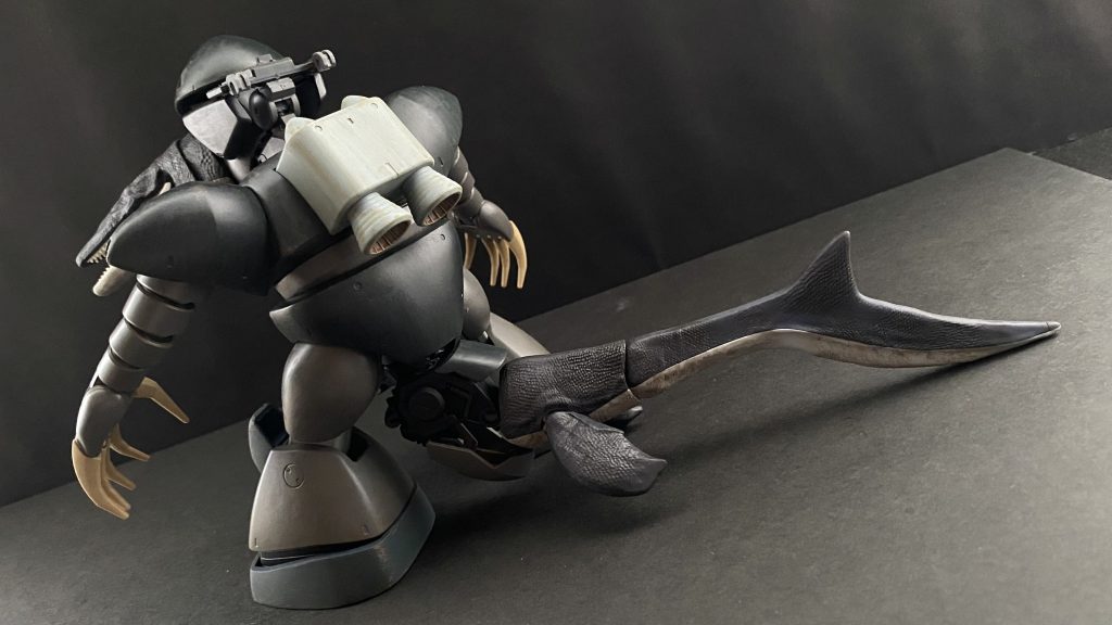 「…報告書は読ませてもらったよ。技術中尉」「はっ」　薄暗い、複数のモニターの明かりだけでかろうじて互いの顔が見えるような部屋の中。敬礼する僕の、机を挟んだ向こう側に座る、技術本部長アルベルト･シャハト少将がゆっくりとこちらを向く。「機体を失うことになってしまいましたが、量産化に必要なデータは充分なほど得ることができました。また、パイロットも無事であり…」「…技術中尉、そのパイロットだが、気になること言っていたそうだな」　シャハト技術本部長が僕の報告を遮る。そう、パイロット。救助されたワシヤ中尉だが、交戦したRX-78に対しおかしな事を言っていたのだ。「はっ、…その、MSが「泳いだ」と、まるで人間のようにクロールで…」「人間の、ように…、か」　そう言って本部長は、手元のパネルを操作し、部屋の一面を締めるモニターの一部に荒涼とした砂漠地帯を映し出す。ノイズが多い、ミノフスキー粒子下のMS戦闘時の物のようだ。本部長はその画面を指し言う。「技術中尉、この映像を見たまえ、ある地上部隊が連邦の木馬部隊と交戦した際に記録された映像だ」　画面の高さ、揺れから判断するに、おそらく06、ザクのメインカメラからの映像だ。映像の奥に交戦相手の姿が見える。白い機体と、赤い機体。…あれはRX-78。「…技術中尉、あちらの、赤い中距離支援機に注目してみたまえ」「赤い機体にですか、…あっ、あぁ、アレは、一体、岩を、岩を投げて、…あの岩はあの機体より質量があるのでは」　自分が今見たものが信じられない。しかも、その後の映像では、06を殴ったりと、赤い機体はまるで人。それも輩のように…。「報告書にあった、「泳いだ」という報告。この記録映像を見る前であったなら、私も技術中尉と同じ感想をもったであろうな」　そう言って本部長はこちらに向き直る。そして静かに口を開く。「このことから、連邦軍のMS技術は、我が軍の技術より数段上をいっている。と言っても過言ではないだろうな」「我々の、我が軍のMSを凌ぐほどの可動性能。それによる「人間」のような動きが出来る。と言うことでしょうか」「…うむ、そう言うことになるな」　薄暗い部屋、重い沈黙が続く。ギシリと椅子を鳴らし本部長は僕に背を向ける。…悔しいと思った。我が軍のMSは、技術は連邦に先駆けこの世界に生まれ、そして数々の戦果を得た。それが数ヶ月で追い抜かれてしまったのか…。握り締めた拳に力が入る。　…その沈黙に耐えきれず、退室しようとする僕の背に、本部長、シャハト少将が声をかける。「…話は変わるのだが、技術中尉。…今回は、モニク･キャディラック特務大尉の、記録映像などは、…無いのかね」　振り返ると、こちらに向き直った本部長と目が合う。「し、失礼ですが本部長。…前回の記録映像は」「うむ、…妻に、見つかってしまってな。…別の、隠し場所を探さねばならん」「………」　僕は、いや、私は、胸のポケットに入っていた、小さな記録用のデータチップを静かに机の上に置くと、ピシリと敬礼し、部屋を後にした。