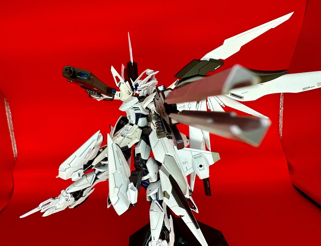 機体解説 01. 戦闘能力 大出力エンジンによる武装の高性能化とスラスター推力増加によって元々絶大な戦闘力を有していた本機は、改修以前から過去の機体を隔絶した性能を秘めていた。 特に速度に至っては特筆すべきものがあり、最大加速時には大気圏内でM12.5、宙域での戦闘機動ではM23.06まで加速し、多角度に設置されたスラスターとフレキシブルに可動するウィングユニットによって速度を維持したまま鋭角的な旋回性能を発揮する事が可能である。 機体やパイロットにかかる負荷も、後述する