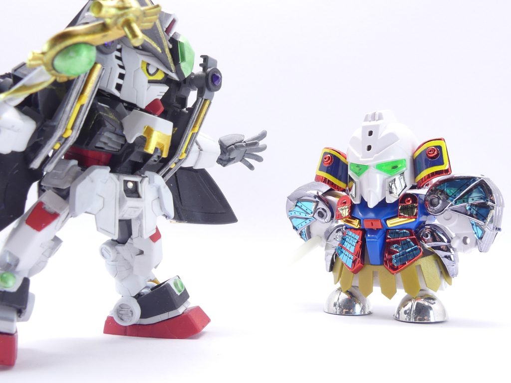 EXissue2「揺るがすニュース」前回のあらすじ:シイナ・アマミチは初めての決闘に何とか勝利・・・しかし、「エバーランド」での冒険はまだ何も始まっていないのです。・・・202X年。世間は夏休み。アマミチ達「ガンプラ部」の3人はテストを無事に・・・まぁ無事に・・・終えたところ。今日は、アマミチの父・マサミチの模型店・「ネバーランド」で今後の作戦会議です。「これが、かつての俺のガンプラだ!」そう言って出してきたのはぼろぼろの武者Zガンダム、それも元祖SDの方!マサミチはかつて、199X年、「エバーブック」を使ってエバーランドにログインし、6人の仲間と共に世界を救ったそうです。当時は携帯とかそう言った時代ではないので、他のエバーブック所持者の連絡先などは交換しなかったそう。しかし、模型店店主として生活するうちに出会った知り合いはいました。コテサシ・ユイ・・・現シイナ・ユイ。アマミチのお母さんに、横浜動くガンダムのチケットをくれたトコロザ・ミツグさん。そして・・・シャクジイ・ゲンゾウさん。「シャクジイさんは俺達のリーダーだったんだよな。二代目頑駄無大将軍を使って戦ってた。憧れもしたよなぁ・・・」マサミチはそう回想します。「シャクジイさんは今、運送関係の会社の社長なんだ。そして、多分・・・他のエバーブック所持者のことも知ってるんだと思う。」「エバーブック」は7冊。今もどこかにあり、そして・・・古本屋に売るとかしなければ・・・かつての所持者は今も大切に所持しているはずなのです。「・・・ま。俺は・・・あんま、思い出したくなかったかなぁ・・・。」マサミチはそう言って頭をかきます。アマミチ達の目標は、「エバーランド」とこの現実世界をつなぐ扉を再び閉じること。謎のログイン者やガンプラもいます、まずはナイトリージョンで手がかりを探すことになりました・・・・・・ちなみにアマミチ達は、シイナ・ユイがかつてのマサミチの仲間でガンプラ婚したことをまだ知りません。当然ながら、彼女の持っていた「エバーブック」のことも知らないのですがこれはまだ先にとっておいて・・・