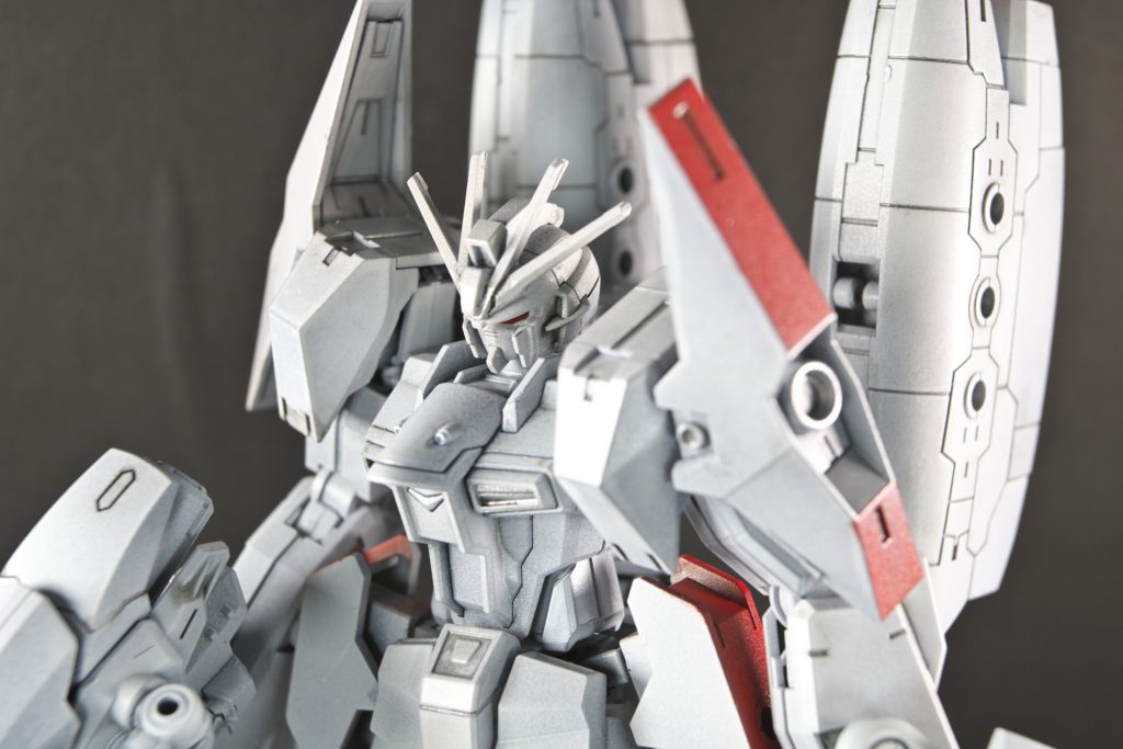 【正面ズーム写真】真っ白っていいですね!洗礼さが出て好きです。刺し色で入れた赤色もなんとなく配合した色ですがイイ感じになりました。友人らからは「消防車!消防車だよコレ!」って言われましたが確かに…いちおう色の配色と色の位置については、機体のエンドが見えないと操縦者が並みのモビルスーツと違ってぶつけまくっちゃうので、それを防止するために塗りました。乗用車を運転する人がハイエースとかのワゴン車乗って擦っちゃうじゃないですか。あれを防止するための分かり易くするための意味合いです。そも狙撃機体ですからね。遠巻きに白色がデブリに紛れていたら、太陽光とかバリ強い宇宙では多分気づけないと思うんですよね。金属片とかチッカチッカしますし。