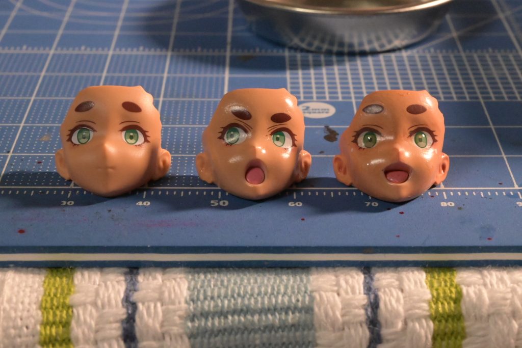 フェイスパーツはピンクサフの上から30minutes sistersボディカラーCで塗装、デカール後にスミ入れ塗料ピンクブラウンでウォッシングし、UV硬化レジンで瞳を作成、ハイライトを入れています。写真は右の笑顔版が完成で、無表情はタンポ印刷で塗装なし、中央は塗装後でこれからウォッシングする前段階です