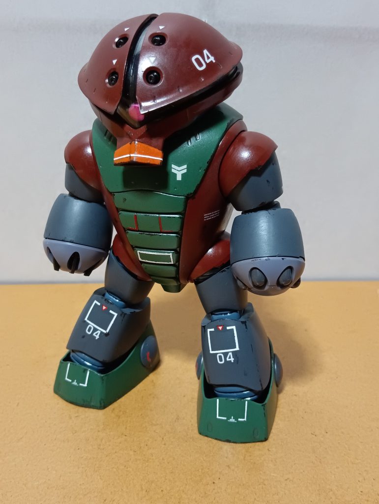 　正面素立ちです。　使用したキットはHGUCのアッガイです。　基本塗装は頭部などがレッドブラウン、腕、脚がニュートラルグレーにツヤ消し黒を混ぜた暗いグレー、胴体と足首が緑にニュートラルグレーを混ぜた少し明るめのグリーンです。　クチバシ（？）はオレンジで塗装しました。　これに、デカールやマスキングテープを利用しての手描きでマーキングを施し、レッドブラウンとグリーンの部分にツヤ消しスプレーを吹いた上から、黒鉄色でウェザリングを入れました。　マーキングはMSVの機体などが載っている雑誌のイラストや、往年の模型マンガ「プラモ狂四郎」に登場する丸山健のアッガイを参考に施しました。　ちなみに、スミ入れはいつも通り基本的に鉛筆とシャープペンです。