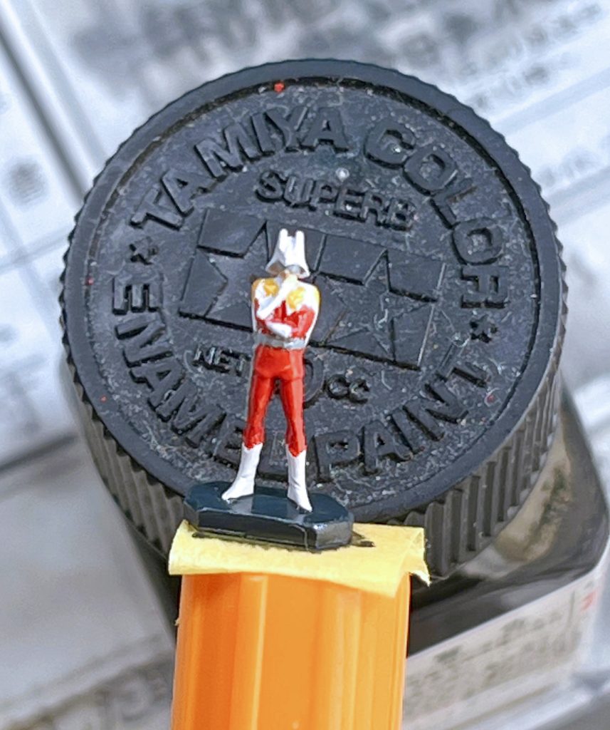 はみ出したら修正して乾燥させたら一旦つや消しトップコートを吹きました。その後にマントの黒色をエナメル塗料で塗り、黄色い肩章部分をジッポーオイルを含ませた綿棒で拭き取りました。綿棒は模型用の先が尖った硬めのものです。最後にスミ入れとなりますが、スミ入れによって塗り分け部分の境界線が誤魔化されていい感じになります。