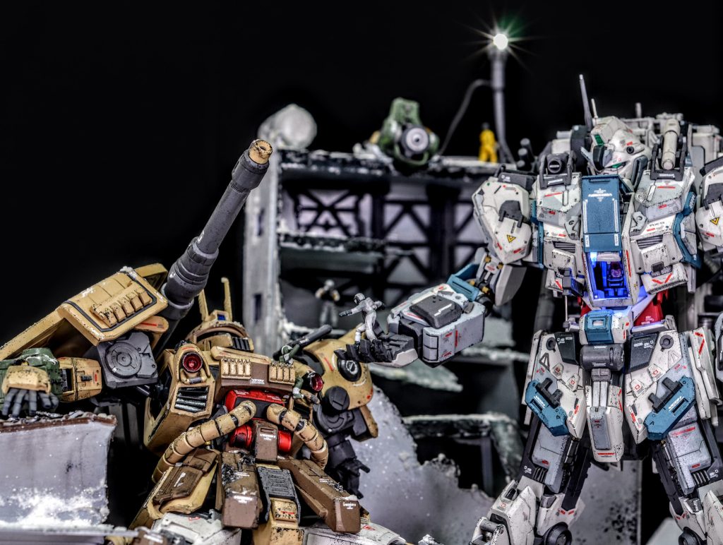 今作の主役のナラティブは少数が正式配備された陸戦装備の特殊仕様で、ザクキャノン改は一年戦争時代のものを20年近く改造し続けた骨董品です被弾したザクは機能停止して擱座しており、その戦いぶりに連邦のパイロットが敬意を表し、敵対者同士ですがコクピットから助け出そうとしています