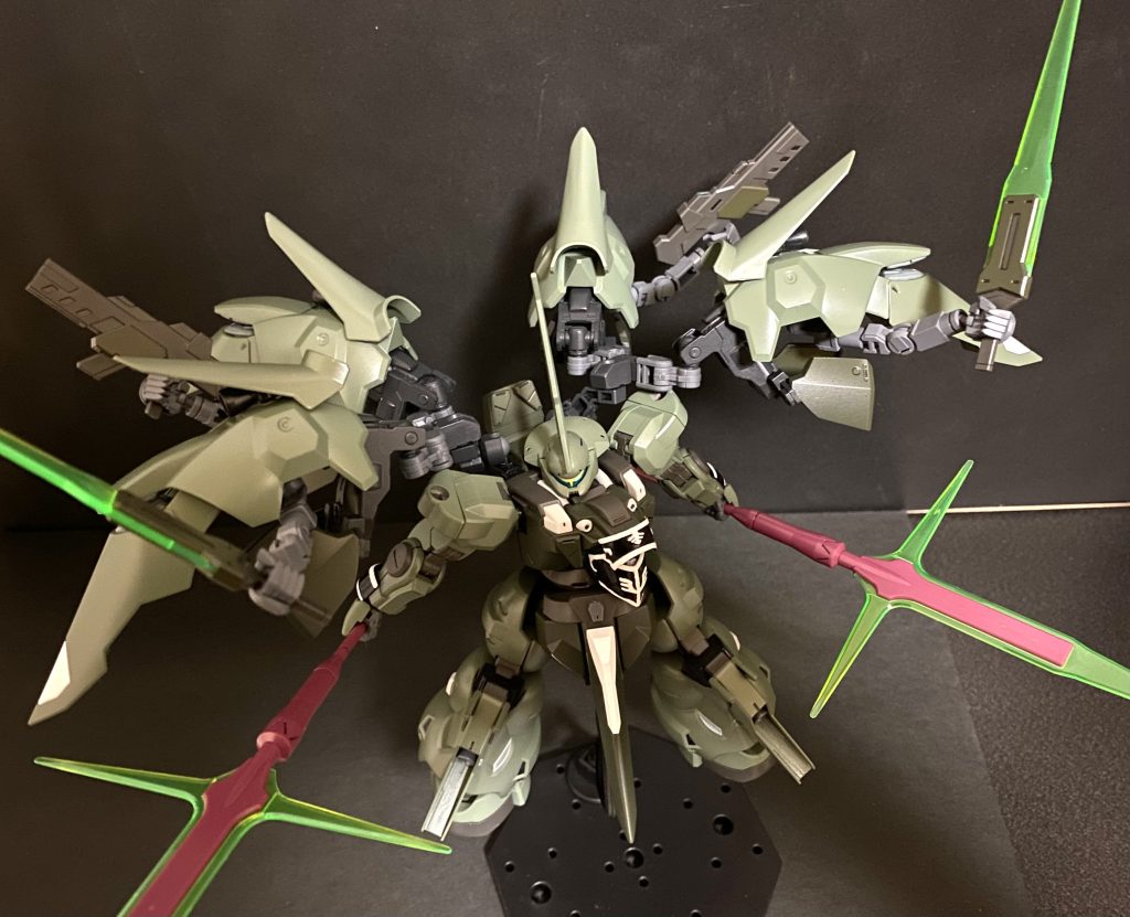 　高速で動くスサノオウのコクピットの中で、グラハムは目を見開き、そして、感嘆する。「その姿…、まさしく阿修羅の如く！」　ディランザ･カッティーヤの四枚の羽、バインダーが展開し、内部に格納されていたサブアームが、それぞれビームトーチ、ライフルを携え、ラージャニヤ。その名の通り、第二、第三の「両腕」として展開される。　突進するスサノオウ。その突進から繰り出されるMSでありながら目にも止まらぬほどの斬撃。それをビームパルチザンが防ぎ、ビームトーチが切り結ぶ。斬撃の隙間は、ビームライフルの射撃がスサノオウの動きを封じる。何度も、何度も繰り返されるそのやり取りは、まるで演舞をしているかのようだ。しかし、それも長くは続かない。「見事だ！だが、今の私は、すでに阿修羅を凌駕しているッ！あえて言おう、私はすでにッ、ガンダムだとッ！」　正面からぶつかり合う二機のMSのスパークが宇宙空間を明るく染める。ビームパルチザンによる渾身の突きは、ブレードによって薙ぎ払われる。しかし、それと同時にビームトーチによる上段からの斬り下ろし。だが、それもブレードによって、返す刃で下から上へと弾かれる。その瞬間、マリィの目に光が宿る。彼女はこの時を逃さない。「この距離だ。躱せるかッ！」　ビームトーチを跳ね上げ、バンザイをした形になったスサノオウの胴体に、二丁のビームライフルの銃口がガチリと突きつけられる。躊躇なく引かれたトリガー。二丁のビームライフルから放たれた二条の光はスサノオウを貫く。　…はずだった。ビームライフルから放たれた「二条」の光。マリィは見た。「四条」の光がスサノオウの背に抜けていくのを。　斬った。斬ったのだ。神速で振り下ろしたスサノオウの二振りのブレードは、それぞれのビームライフルから放たれたビームを斬ったのだ。その切先はライフルの銃口も切っていたのだろう。小さな爆発が起き、ディランザの動きが止まる。グラハムはその隙を逃さない。スサノオウの両の手のブレードが十字の軌跡を描く。　爆発が収まった時、そこには、根本から切り離されたディランザ･カッティーヤのツノ飾り、ブレードアンテナがあった。 