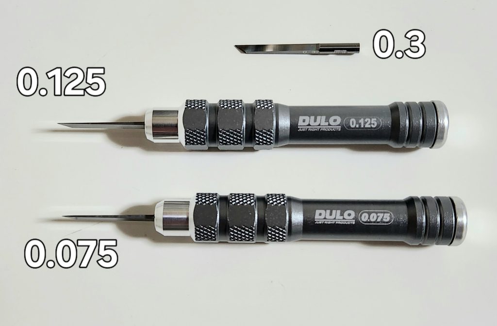 今回のスジボリはレイウッドさんのDULOタングステンブレードを使いました。BMCタガネを落として折ってしまったので買い足そうと思ったけど入手困難(2024年2月当時)だったので、こちらを買ってみました。タングステンブレードは刃先が台形なので1番細い0.075でも掘り始めが難しいでしね、BMCタガネとの感覚の違いに慣れが必要な感じです。タングステンブレードの刃先は台形なので掘るほど幅が広くなりやすくなるのでタングステンブレードの0.125がBMCタガネの0.15と同等の太さかなって感じです。タングステンブレードは刃が太いので直進性は高く1回での彫り込み量も深いのでハミ出したりミスった時のキズも深くて修正が大変でした。専用グリップは見た目も良く持ちやすいですね。刃先だけでも購入出来るので使用頻度の低いサイズは付け替えの手間を惜しまなければ複数サイズを揃えやすいので、次は0.15と0.2が欲しいですね。でも最初から5本セットを買うのがコスパ良いですがね^^;と言いつつ量産型BMCタガネも気になってますが。