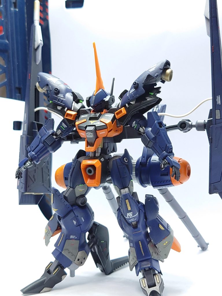 〜怪鳥の翼持つ 巨人の尖兵〜バスク・オム麾下の特務部隊「ネフェリム」に増援として編入された戦力。先行量産型のバーザムをベースに既存の技術を導入した高機動追撃仕様として完成している。開発にはティターンズ技術陣営のみならず出向中のジオン系アナハイム技術者が加わっており、過去にアナハイムが開発した機体の設計が組み込まれているとされる。最大の特徴は背部ドラムフレームに直結したフレキシブルフレーム、これを介して接続されたギャプラン由来のムーバブルシールドバインダーである。高高度迎撃機とされるギャプランに匹敵する推力を生み出し、シールド ブースター ビームガンの機能もそのまま継承している。エゥーゴ・カラバとの交戦が激化する情勢において早急な戦力を必要としたティターンズ前線の要望によって開発が開始。初期構想ではガルダ級の艦載機として運用することとされたため、ヒンドゥー教におけるガルダの別称として「スパルナ」と呼称されるに至った。その高い機動力は重力下では短時間の推力飛行、宇宙空間では超高機動戦闘を可能にする。半面、重力下での飛行はギャプラン同様推力に依存したものであり、パイロットに掛かる負担は空気抵抗をあまり考慮していないデザインも相まって「殺人的」な領域となっている。同様に推進剤の消費も激しく、ピーキーな仕様も相まって「強化人間」による運用が推奨されている。