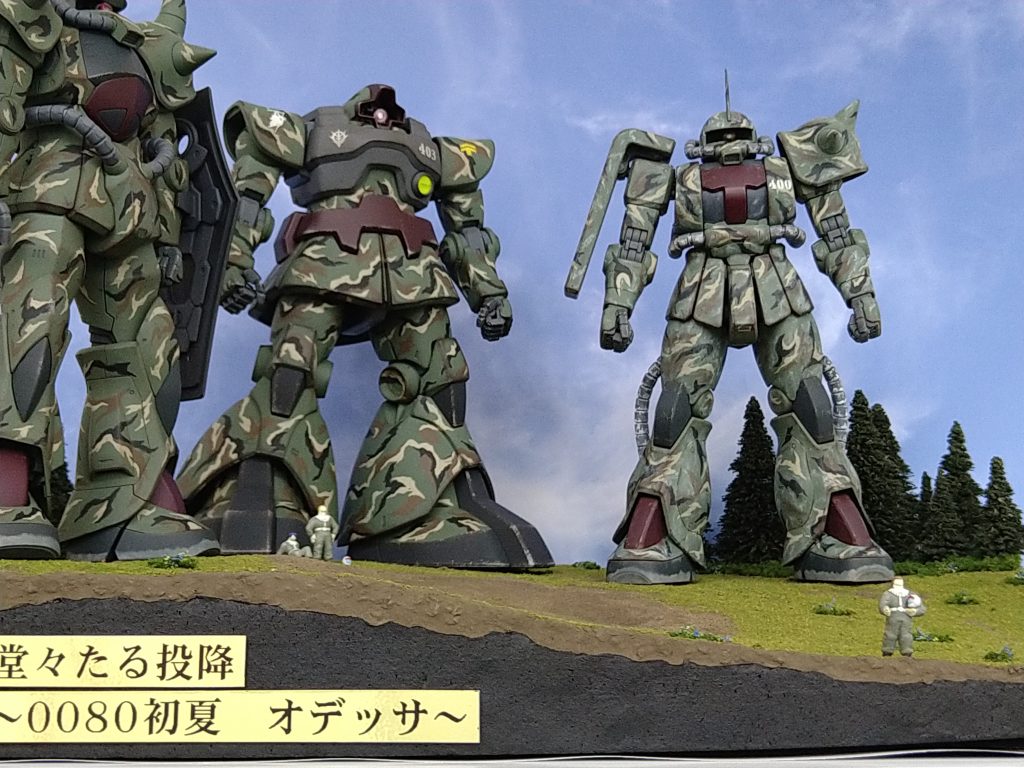 ジオラマ全景。オラザク応募時から撮り直した全景です。応募時は色々あって作品完成が締め切り当日ギリギリで、撮影に時間をとれず『やっつけ仕事』になってしまってたので、少しはマシになったかと😁★さて、登場キャラが写真内にそろいましたので、機体及びパイロットの設定も記載します。ちなみに、右端で握手の右手を差し出しているのがルトガーさん、左端で足を投げ出して座っているのがクンツさん、その隣で清々しく空を見上げるのがデニスさん、です。【機体番号400】 階級:大尉 氏名:ルトガー・イーハトーヴ 乗機:MS-06J 設定:34歳。男性。 寡黙だが隊長として果断に富む。MS操縦の技量は非常に高く、重力下での運用センスは圧巻。射撃と近接戦闘、共に絶対的な技量を持つ。 部隊に新型機が配備されてもすぐに部下へ渡してしまう等、部下思い。口下手であるがその行動で部隊員から慕われている。始祖は東洋の出身とも。【機体番号401】 階級:大尉 氏名:ヴァルター・オイゲン 乗機:MS-06J 設定:32歳。男性。 MS戦闘に関する技量は高いが広い視野で現場指揮官としての能力も高く、後方からの支援と部隊の誘導を担当。 バランスのとれた性格で機転も利き、副官には非常に適した人物。オデッサ作戦の熾烈な退却戦で惜しくも戦死。機体も大破、放棄された。【機体番号402】 階級:軍曹 氏名:クンツ・バウアー 乗機:MS-07B 設定:27歳。男性。 皮肉屋であるが、合理的な性格の持ち主。小柄で非常に俊敏。近接戦闘では抜群の成績を収め、模擬戦ではルトガーに勝利する事もある。 好き嫌いが露骨に出てしまう為に扱いづらい人物であるが、ルトガーには心酔しており、オデッサ陥落後も部隊に貢献を続ける。【機体番号403】 階級:中尉 氏名:デニス・アーベル 乗機:MS-09 設定:30歳。男性。 明るく社交的な性格で士官学校時代から常に成績優秀。上官にも可愛がられるが、信義に沿わない事へは態度を明確にする面があり、今ひとつ出世は出来ないでいる。
