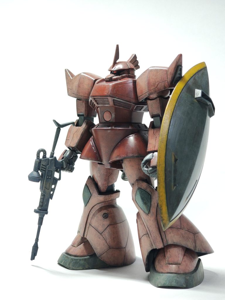 盾持ち。ライフル、ビシっと持ててないですね。塗装レシピ。メカサフヘビィ後、ほぼ全部、水性ホビーカラーです。ピンクが難しかった。濃い赤: あずき色 > モンザレッドピンク: サーモンピンク > シャア専用ピンク盾とサーベルの黄色: ハイネ専用オレンジ > ガンダムイエロー膝、靴、縦の中央:  グレーバイオレット> 軍艦色1関節、盾の裏: サフ > 明灰白色1スカート内のバーニア:  エナメルのチタンシルバー+バーニア内側クリアレッド (写真ないけど)濃い赤のモンザレッドは馴染みすぎていて、もっと違う色が良かったですね。 この後、半光沢トップコート > ダークブラウンウオッシングしましたが、二色目のハイライトがだいぶ消えてしまうので二色目もウォッシングも加減がわかりません。あと、ゲルググといえば、テキサスコロニーなので砂っぽい汚れを足元、スネの下の方だけ足しました。