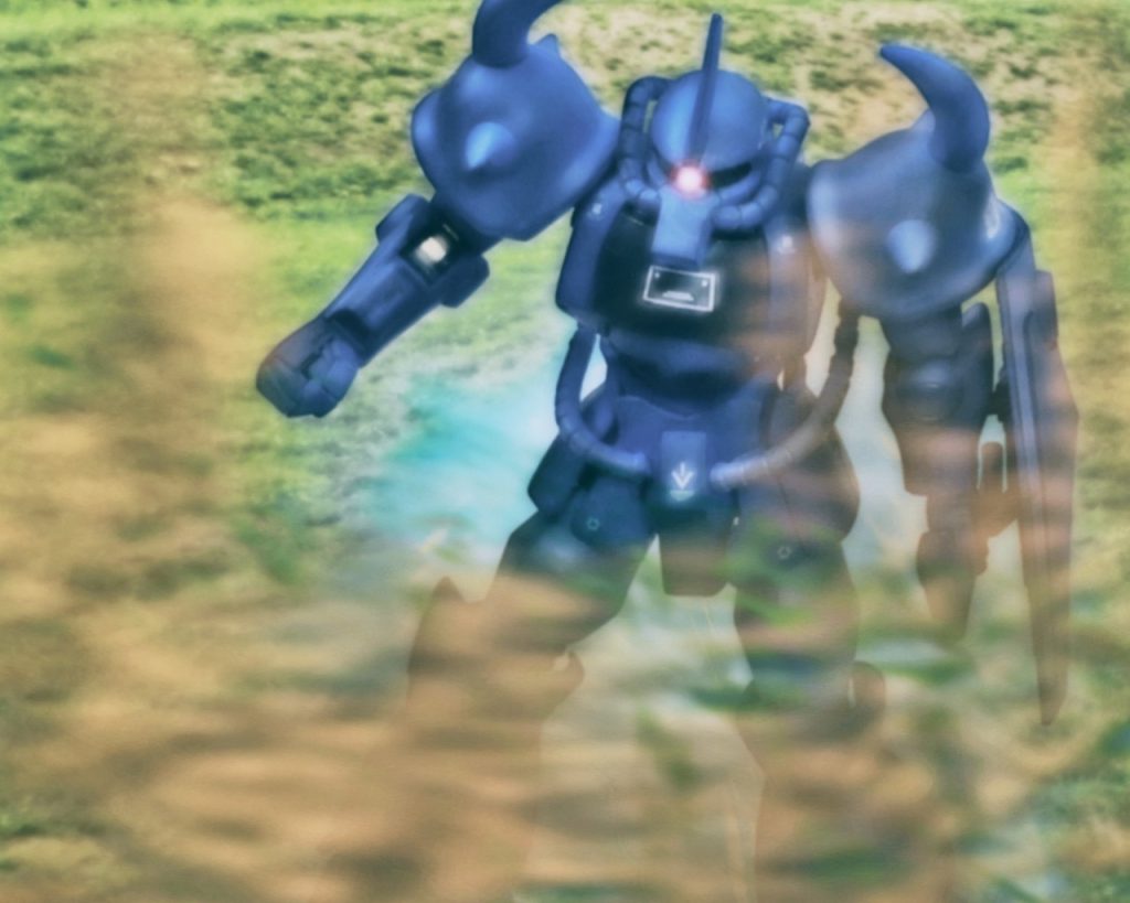 「…距離1000。スラスター全開」ラカンはスロットルレバーを押し込み全てのスラスターを噴射させる。それとほぼ同時に身体には巨大な岩が押し潰すように重圧が掛かり、生半可なパイロットではこれに耐えられず気を失ってしまう。だがコールサインさながらラカンの強靭な肉体はこれをものともせず耐えた。「…距離200、150、100、50、…着陸」脚部が衝撃を和らげるよう着地と同時に関節部分を屈曲させる。轟音と共に砂煙を舞い上げグフは着陸したが、直ぐ様戦闘態勢に入る。これだけ砂煙を上げればレーダーだけでなく、目視でも敵に位置を知らせているようなものだ。ラカンは敵基地を座標中心に周囲の状況を確認する。「敵MS3、車両1、接近中。降下中に見えた連中か」接触の早さから恐らく基地からスクランブルで出たのではなく、警戒中の部隊と遭遇戦になったと考えられる。