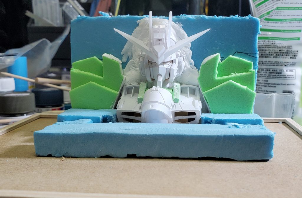 白サフからの百均スタイロフォームで作った壁に後ろ半分をめり込ますように配置、肩や首周りの隙間はスチレンボードで形作りました土台も百均の箱です。