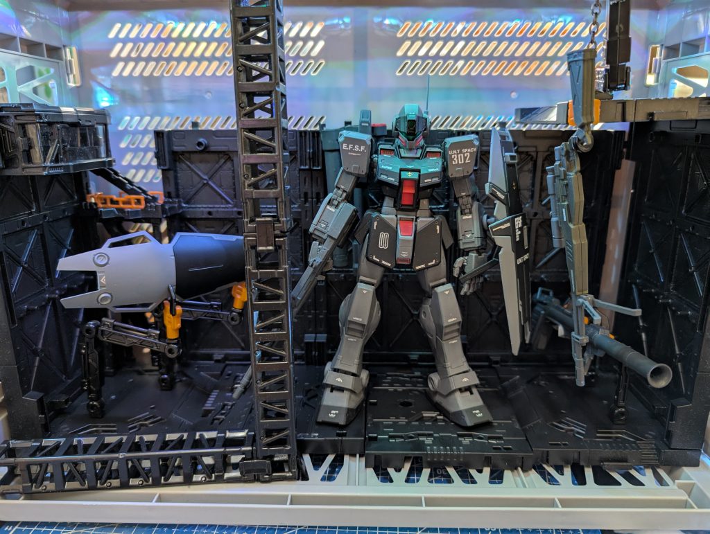 余った装備とMSハンガー風に昔、アミューズメント施設で稼働していたガンダムカードビルダーに相当入れ込んでおり、私はしょっちゅうリド・ウォルフ中尉を隊長にジムスナイパーⅡを出撃させてプレイしていました。基本となるモビルスーツに様々な武装を持たせる事が出来て、気に入っていたのはジムスナイパーⅡにアレックスのビームライフルにシールド、テスト用EXAMシステムを装備させ、追い詰められるとジムスナイパーⅡのカメラが赤く光り、クリティカルを出すとリドが「黒い死神の死の踊り、見せてやるぜ!!」と喋ってくれるのがサイコーでした(gundam-kao3)
