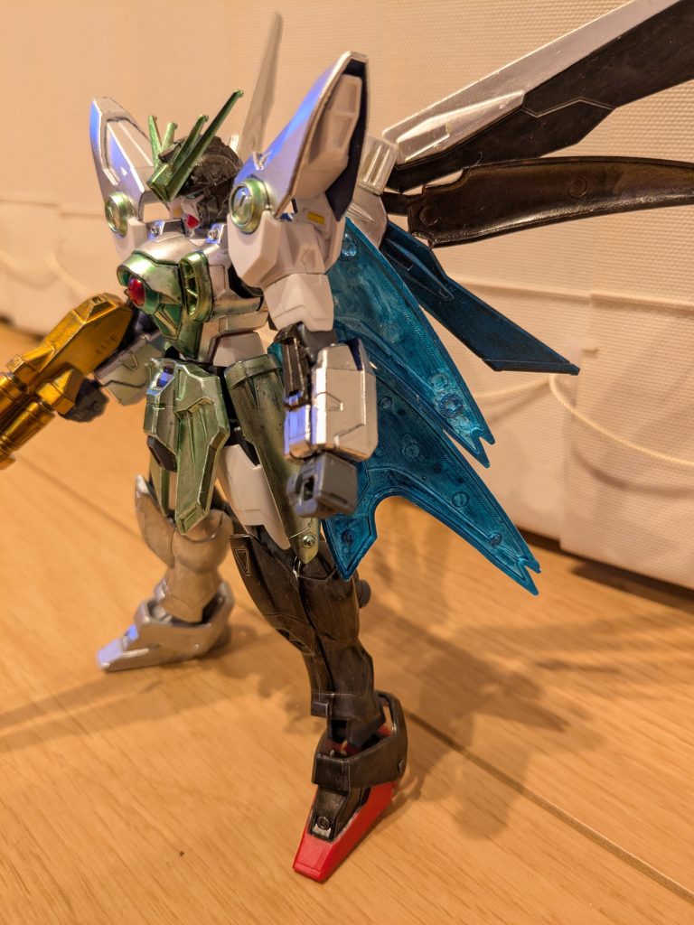 左サイドショット肩、腕の青い部分はシャインシルバーで黄色の丸の部分はメタリックイエローグリーン、腕のクローはメタリックブラックです。左足は分解の足をイメージしてメタリックブラックで塗装。つま先は成型色のままです。ウイングは黄色の部分をシャインシルバー、白の部分をメタリックブラック、赤の部分をコスモメタブルーです。これだけでも良かったんですが、もっとお空のボリュームある羽とマントの感じを出したいと思い、旧キットガーベラテトラのリアバインダーをメタリックブラックに塗装して羽の間に差し込み。旧1/100ヘルカスタムの肩の白い部分を半分にして組み合わせ、内側をコスモメタブルーに塗装し、リアスカートとサイドスカートの間に差し込み、マントっぽくしてみました。