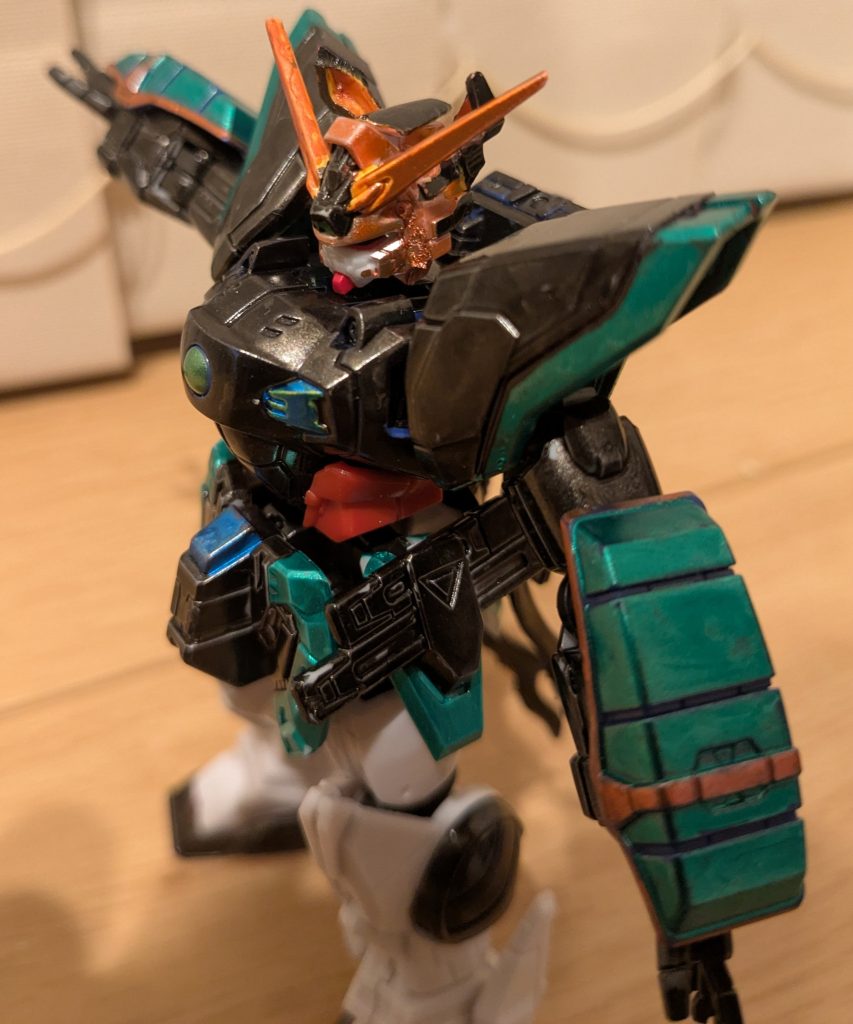 バストアップを１枚。頭部は、髪をイメージしてメタルレッドで塗装。アンテナも、おさげイメージで同様です。頭部中央とシャイニングのたてがみ部分は、お燐のリボンイメージでメタリックブラックです。で、輝夜ストライクを作ったときに出たストライクのシールドの余り部分を後頭部に接着し、中をメタルレッド、外をメタリックブラックに塗装することで、お燐のネコ耳にしてみました。余り部品なんだけど、ちゃんとそれっぽくなって良かったです。ボディはお燐の服をイメージしてメタリックブラックで、その模様をイメージして、黄色の部分や腰中央の赤い部分をメタリックブルー。腰回りの赤の部分は、帯をイメージして成型色のままです。肩の赤い部分や腕のアーマー、スカートの周りは、お燐のフリルをイメージしてメタリックグリーンにしました。腕アーマーのメタルレッドは、腕に付けているリボンのイメージです。