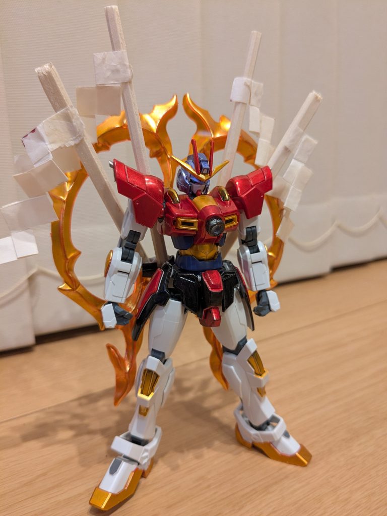 まずは素立ちで１枚。頭は髪イメージでメタリックバイオレットと、頭に巻いている注連縄をイメージして、メタリックオレンジとロイヤルメタレッドです。体と肩はロイヤルメタレッド、スカートはメタリックブラックと、ポイントをロイヤルメタレッド。あとは全身に巻いている注連縄と草履をイメージしてメタリックオレンジで塗装。胸の丸パーツは、鏡をイメージして、Gframeの固定肘関節を切り出し、外はメタリックブラック、中はメッキシルバーで塗装したものです。背中の大きな注連縄は、メタリックオレンジに塗装したカミキバーニングの炎エフェクトを使用。で、背中に一緒に付いている御神木。木の質感を出したいと思い、割って半分に切った割り箸を使用しました。そこに元霊夢ストライクのお祓い棒の紙を貼り付け、装着してあります。このおかげでしっかり加奈子の雰囲気が出たと思います。