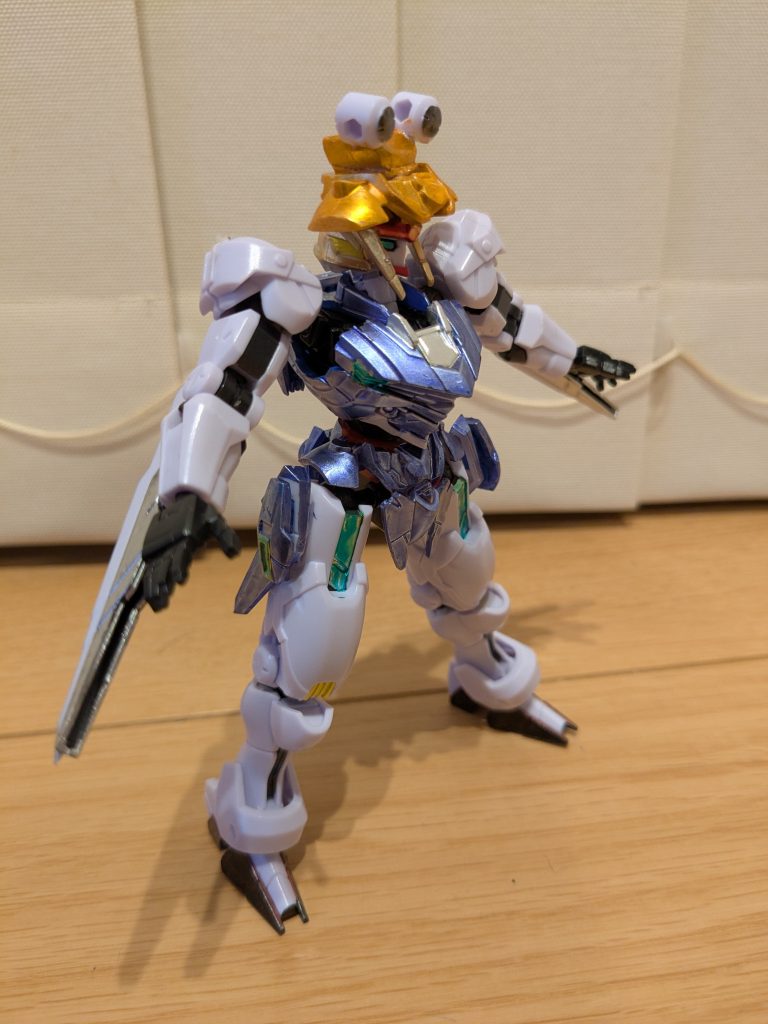 サイドショット。ガンビットの長いやつを肘に接続して黒、青の部分をシャインシルバーに塗装し、諏訪子の袖に見立ててみました。同じく首元をシャインシルバー。体は背中と同じくメタリックバイオレット。服の模様をイメージして、右胸の黄色部分と足のパーメット部分をメタリックグリーンにしました。左胸の黄色部分は、結び紐をイメージしてロイヤルメタレッドです。頭部では、サブアンテナを切ってメインアンテナに下向きに付けてイエローゴールドに塗装したことで、諏訪子のまとめた髪に見立ててみました。そして帽子。固定フレームの腰回りに付けた肩関節部分の中央をメタリックブラックに塗装したら、しっかり諏訪子様になりました笑