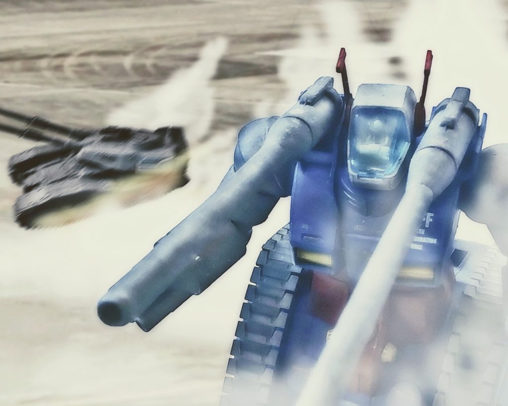 「機体130度旋回、対空戦闘用意!」地球連邦軍の長距離支援試作MS、RX-75ガンタンクは排熱の白煙をあげながら砲身を上空へ向けた。このガンタンクの有効射程距離は現行のMSとしてはトップクラスである。地球連邦軍の試作MS群の中でも下半身がキャタピラという異型な形ではあるが、陸戦兵器としては他に類を見ない程、有能であった。隣にいる61式戦車と比べてもその大きさからMSと分類しても差し支えないと言える。この様な拠点防衛戦では移動できる長距離砲台として対空、対地両方に対応可能であり、火力の高さから陸戦艇にも致命傷を与えられる。ウィークポイントとして近接戦闘に対応しづらい事だが、そこまで近づくのも容易ではない。「砲撃準備開始。敵目標480ノットで移動、気温15℃、風速3メートル、自機5ノット、射角42度に設定」ガンタンクは基地の周りを飛ぶドダイYSに狙いを定めると、120ミリ低反動キャノン砲が火を吹いた。「砲炎確認!回避運動!!」ドダイは急旋回しGに耐えると、機体すぐ横をガンタンクの砲弾が抜けた。「この距離を狙うかっ!?なんて野郎だ!」ペアを組んで飛行していたドダイは散らばると、一旦基地から離れる。「リンドヴルムリーダー!敵はそれだけじゃない!そっちに新たなMSが向かっている!かなり早いぞっ!」「まだいるのか!?何機だ?」ビリーはストークリーダーに聞くが、無線からは雑音が強く聞き取れなかった。