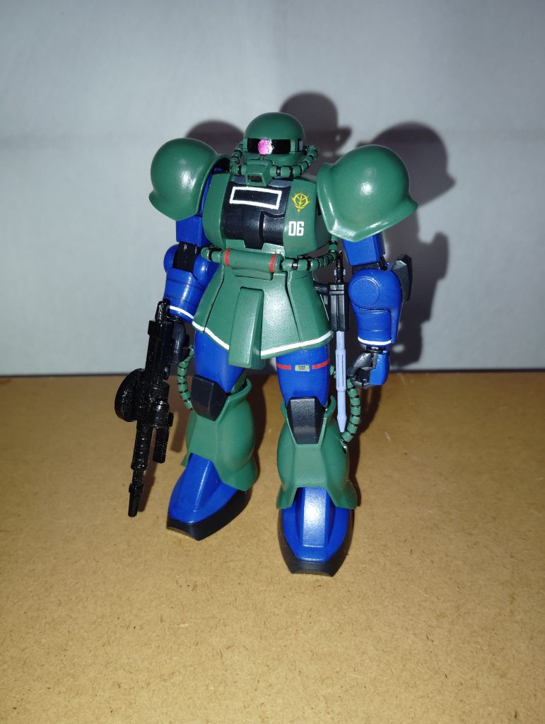 正面素立ちです。 使用したキットは旧HGUCの量産型ザクです。 右腕ショルダーアーマーや手首は、前回投稿したザクⅠ(ランバ・ラル機)と同様ザクⅠスナイパータイプから流用しました。 基本塗装はインディブルー、緑にニュートラルグレーを混ぜた少し明るめのグリーン、ミッドナイトブルーです。 マーキングですが、胸部やスカートまわりなどの白線、動力パイプ基部や左太ももの赤線はマスキングテープを利用して手描きで再現しました。 ジオンマークや数字、コーションマークなどはデカールやシールです。 マーキングを施した上から、仕上げにツヤ消しトップコートを吹いてあります。 モノアイはいつも通り、銀色で下地塗装をした上からマッキーのピンクで塗ってあります。 ちなみに、スミ入れはいつも通り基本的に鉛筆とシャープペンです。 そういえば今回の塗装ですが、MSV-Rにて公開された設定イラストとは微妙に塗装パターンが異なります。 私が参考にしたのは、かつてゲームセンターで大盛況し、惜しまれながら15年以上続いたサービスが終了するも、続編(?)となる「Ⅱ」が大爆死したアーケードゲーム「戦場の絆」に登場する機体です(機体と言っても、ゲームの攻略本のオマケとして封入されたザクⅡの色違いバージョンという扱いですが)。 個人的には大河原邦男先生が描いたイラストのバージョンより、こちらの旧型ザクとほとんど変わらない塗装に惹かれたので、今回はコチラをチョイスしてみました。