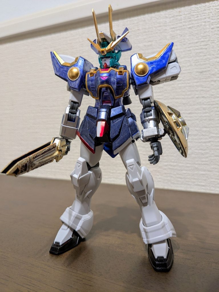 素立ちで1枚。ボディは背面と同じ配色です。体中央のポイント3カ所ほどメタリックピンクに塗装し、服のボタンイメージにしてみました。スカートも同様に、右下部はロイヤルメタレッド、左下部はシャインシルバー。中央下部は真ん中でスジ彫りして、半分はロイヤルメタレッド、半分は成型色のままです。で、四季様の武器「悔悟の棒」をイメージして、エピオンパイを作ったときに使わず、グリップのなくなったMGエピオンのビームソードに、EGガンダムのビームライフルのグリップを付け、イエローゴールドに塗装。100均のデコレーションシールを必要分カットして貼り、それっぽく作ってみました。シールドは、四季様の持つ「浄玻璃の鏡」をイメージし、側をイエローゴールド、中央をメッキシルバーで塗装し、ドラゴンハングを付けるための部分に差し込んであります。