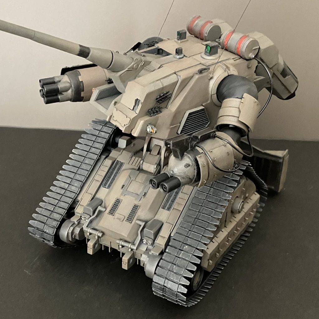 2次元の立体化にあたり、資料を参考に縦横長さの比率計算しつつプラ板にて作成しました。パテ使用は肩パーツの造形と隙間埋め程度です。カラーリングはCG画像では作成当初、グレーだと思い込んでいましたが、よく見るとサンドカラーでアニメを観てやはりサンドと確信。色弱なんで笑。本体塗装は缶スプレーのタミヤTS-4ジャーマングレイを下地にタミヤアクリルXF-72茶色(陸自)にXF-63ジャーマングレイを少し混ぜたものを筆塗り。履帯はTS-6フラットブラックの上からTS-48ガンシップグレイをうっすら吹きかけ。ドーザーブレードはTS-100ブライトガンメタル。塗装後、Mr.ウェザリングカラーのステインブラウン、グランドブラウン、ウェザリングパステルのサンド、チャコールブラックにて汚しました。