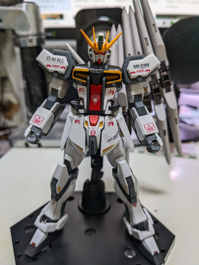 まずは、元となった、ガンプラ作品を作り始めて、2作品目となる『EGストライクガンダム』ですが、これは2022年4月にXにて投稿した作品であり、かつ初めてガンダムマーカーを使用して色をオリジナルカラーにした後、水転写式デカールを貼り、楽しくオリジナルガンプラを作れた最初の作品でした。今改めて見ると、当時はマーカーと筆塗りだけでしたので塗装が厚ぼったく、デカールも貼ることで印象がガラッと変わったことに楽しさを覚え、これでもかとデカールを貼っている作品で、今改めてみるとうるさいイメージが強い作品でした。良く見るといつの間にかアンテナも折っていましたが、当時は全く気がつくこと無く、また飾る手段も当時は持ち得なかったため、作った後はそのままガンプラ箱にしまい込んでいました。ですので、今回は出来るようになったこととして、塗装を見直し、ネオジム磁石工作を若干ですが行い、また余剰パーツも増えたのでそれを利用し全体的なデザインを変更した後、個人的に苦手な部類に入っている「スジ彫り」と向き合って、今持っている道具と技術でリメイクを行いました。