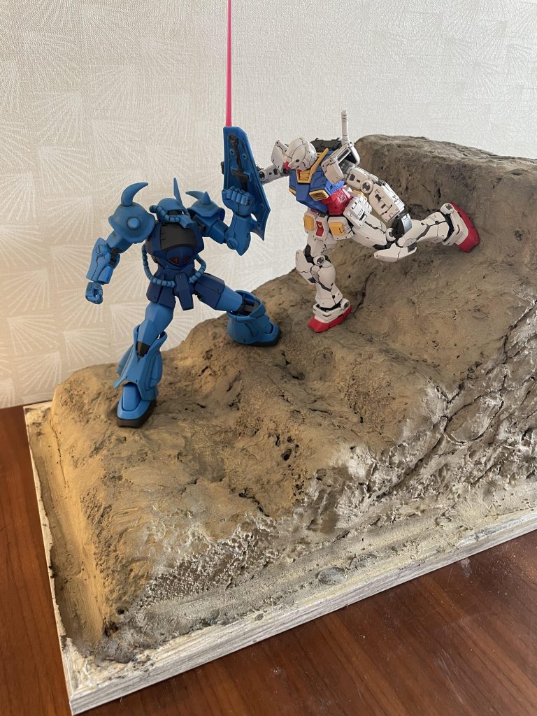 ジオラマ全景です。(縦30cm*横20cm: 一番高いところで20cm) ダイソーの発泡レンガを合計7個組み合わせて作成しました。ツールクリーナーを使用し各レンガの合わせ目を溶かした上で表面に粘土をうすく塗りつけています。ウェザリングカラーのサンディウォッシュで塗装しています。登場人物(MS)の入れ替えのみで劇中の様々なシーンに対応できるようベースの汎用性を高める事を意識しています。当ジオラマ土台を用いてガンダムとシャア専用ゲルググの斬り合いシーン(ゲルググがガンダムの上からナギナタを振り下ろすシーン)の表現を計画中です。
