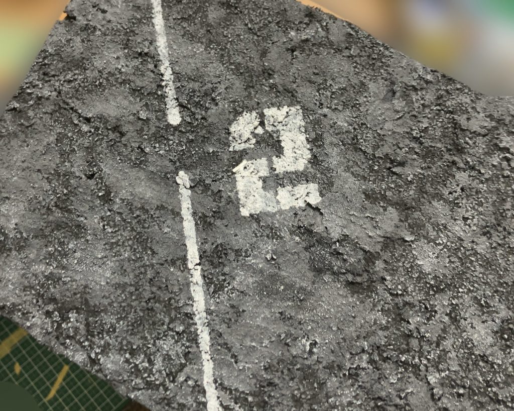 ジオラマのアスファルトの部分のの写真です！初めてアスファルト作りにチャレンジしてみたのですが、白線を引いたり、ヒビ割れた箇所にスミ入れをしていく事で、どんどん本物の様な質感になっていくのが楽しかったです😊