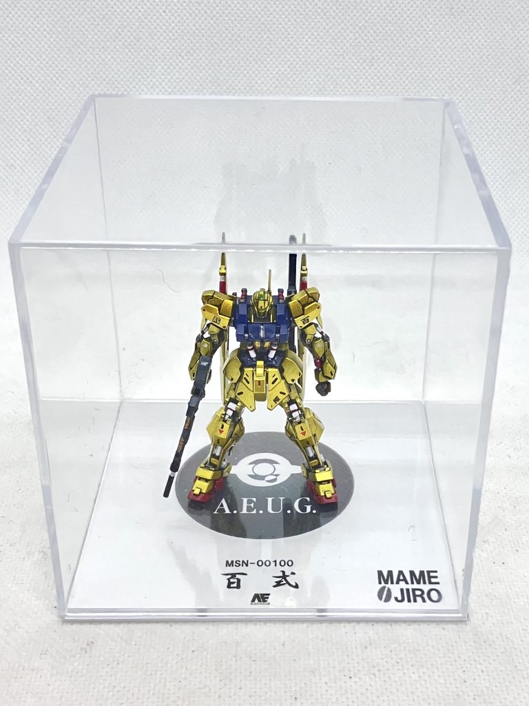 　ディスプレイ用のケースはセリアのものを加工。１ミリプラ板にエゥーゴマークを印刷した紙を貼り、その上にケースを置きます。足の裏に2ミリプラ棒を貫通させて差し込めば、しっかり固定できるのがミソです。