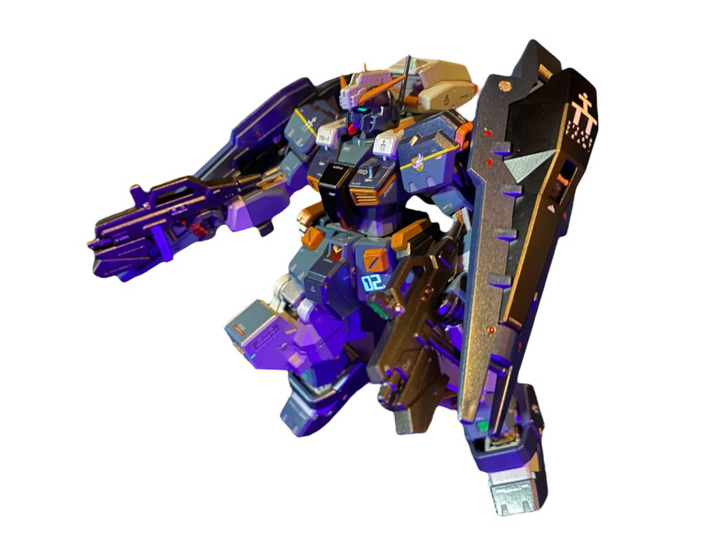 「ヘイズルは1号機も2号機も改装作業中か?」ヘンドリック主任の元でずっとヘイズルの面倒を見てきたメカニックのピート・シェルトンが答える。「イズミールの格納庫はここにくらべりゃ狭いからさ。乗り移る前に塗装なんかはこっちであらかたやって来て来れだとさ。だから今日は機体を拝めなくて残念だったな。」「いや、今日はMS見に来たんじゃない。世話になったメカニックのみんなに一言礼を言って行こうって話しててさ。本当に今日までありがとう。」「ここに来てからというもの、毎度毎度新しい機体を用意してくれて、整備班のみんなも本当大変だったと思うぜ。」「カールは機体を良く壊してたしな〜!笑」「そりゃ〜しょうがねぇじゃねえか〜!ジオン残党はしつこいし、技研の連中も無理言うし〜!」「あんたらのしょーもない会話も聞けなくなると思うと寂しいもんだな!笑まぁ、俺たちは俺たちの仕事を責任を持って当たり前にこなしてただけだ。今日までも。そして明日からもな!“ガンダム”を、あんたらの機体を手掛けられたこと、『誇り』に思うぜ。あっちに行っても、また絶対に帰ってこいよな。この船は俺らの家みたいなもんなんだから。」「あぁ、ありがとう。必ず帰ってくる!ヘイズルと共にな!!」ピートとエリアルド達は熱い握手と抱擁を交わした。「明日にはこいつの塗装も終わるからさ、そん時にあんた達、記念写真でも一枚どうだ?いずれ実戦仕様としてTR-1も再配備される。そうなりゃコイツらも一緒くたにティターンズカラーさ。その前に、なつかしいカラーリングに一度戻してやろうと思ってね。まぁ、俺たちアスワンのメカニックチームの『誇り』ってやつをイズミールのクルーにも見せつけてやりたいのさ。」