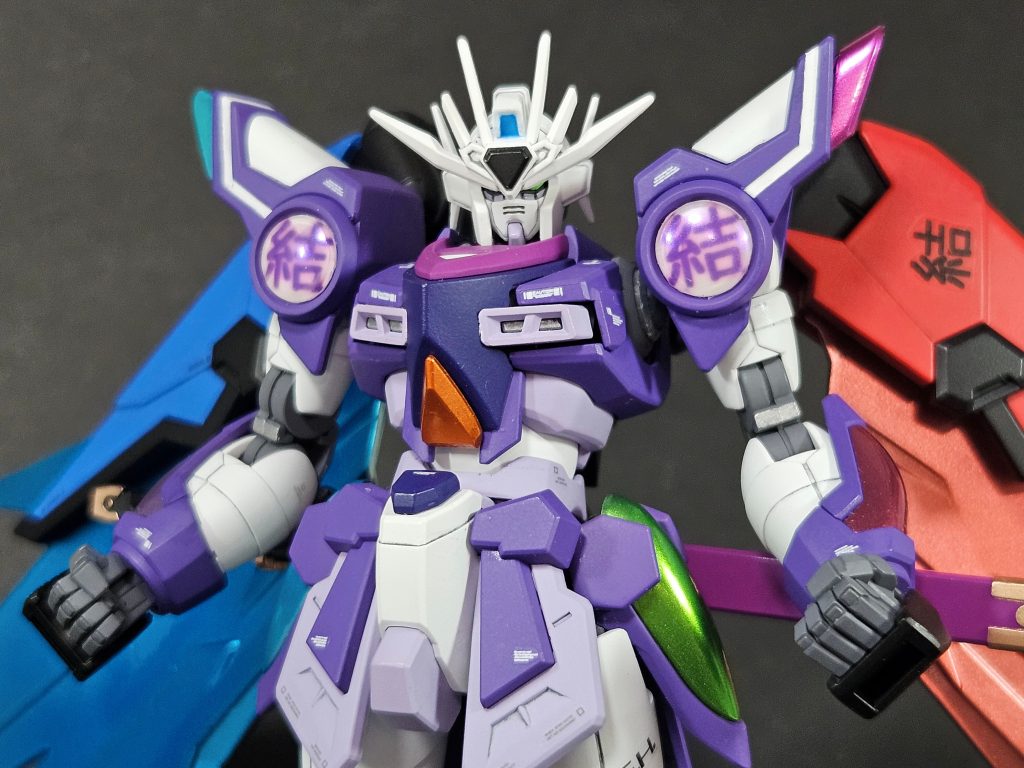 ジャキーン中から紫のガンダムが出現し、本来の姿となります。「結」（ユイ）の文字は、主人公たちのスクールアイドルグループLiella!が所属する結ヶ丘女子高等学校を表します。また、