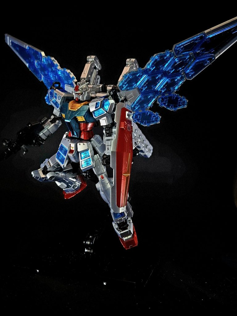 その様子はあたかも新型のガンダムを開発していくようなプロセスであり、開発の約2年後に起動実験が行われることとなる。なおパイロットについては特に設定が明かされていないものの、「F00 /AI Awakening!」における演出で「金色の髪と青い瞳」を持っている事が分かる。