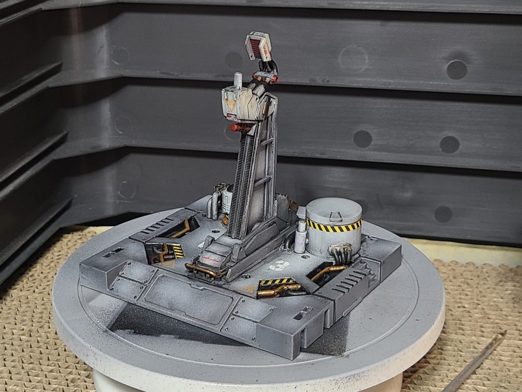 100均の格納庫は最終的にこうなりました。格納庫底面にプラ板の支柱。その回りに適当にジャンクパーツなどを配置してそれっぽい雰囲気を演出(笑)支柱前面のギザギザは、結束バンドです。上の接続部分が上下に動くためのレールのように見えたらいいな、と。