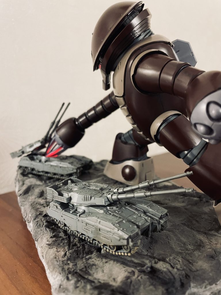 劇中61式戦車を右のクローで撃破するアッガイをイメージしています。61式戦車はHGザク地上戦セットからの流用です。造形がしっかりしており細部に渡りディテールが再現されています。ウェザリングカラーのマルチブラックを全体に、キャタピラ部分にマッドイエローを使って汚しを入れています。