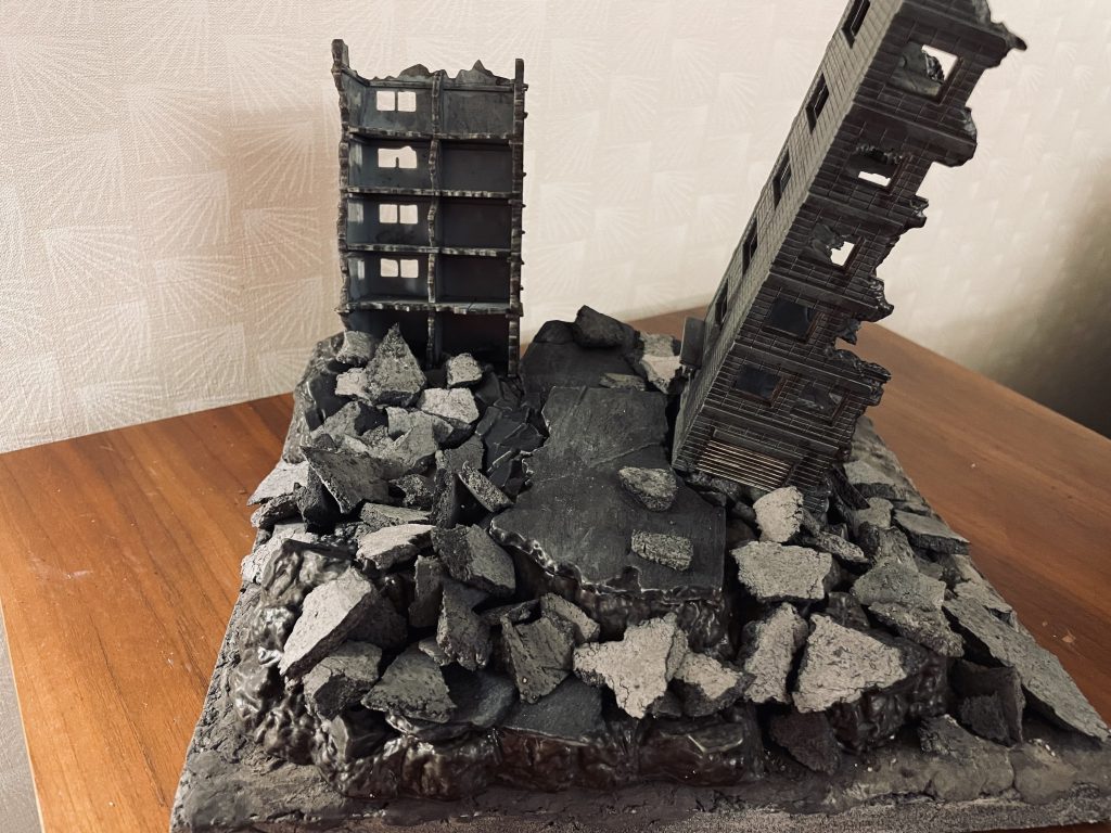 ジオラマベース全体です。瓦礫は100均の灰色粘土を平らにのして乾燥させた後、適当なサイズに砕いたものです。固定はせずにベース全体にばら撒いています。マルチブラックでウォッシングをしていますが、裁断面は灰色のまま残りますので、再度全体にマルチブラックを塗布して整えました。中央のやや高めのビルはトミーテックからの流用です。