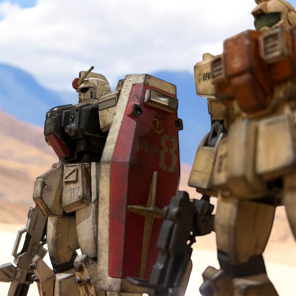 「V作戦ていうのは、あれはどうなっているんだ。サイド7が攻撃を受けたっていうが……。」黒鉄の巨人、MSを見上げながら、イギー・ドレイク少尉が呟く。「少佐の話じゃあ、なんとか脱出して、母艦ともども遊撃任務に就いてるってさ。地球に降りてきて、この辺で戦ってるんだろ。」ヘント・ミューラー少尉が、呟きを受けて答える。「うちのMS開発はV作戦のデータを受けてって聞いてるんだが、さっきこいつらの中身を覗いたが、これは……」 そのデータと思しきものは、機体の中に存在していない。テストばかりの実戦経験もない“空っぽ”の頭のまま送り込まれていた。「待ってられないんだろ、彼らのデータを。ジャブローを経由しなくちゃさ。その前に、オデッサ・ディがやってくるよ。」「だからだろ、ここまで歩いてくるのも一苦労だ。こいつら、地球の歩き方も知りやしねえ。こんなんでジオン星人と戦えるのかよ。」だと言うのに、地上では必要ないと思われる、宇宙での姿勢制御機構のデータなどが紛れ込んでいる。宇宙でのテストの名残だろう。 イギー・ドレイクと、ヘント・ミューラーは、オデッサ作戦に極秘投入されるMSの、パイロットとして配属された。しかし、当のMSは、本来の開発計画の規格から大きく外れて開発されたもので、とても実戦に役立つものとは思えなかった。 本来V作戦の開発機体群のデータを基に開発が進められるはずだった連邦製MSだが、そのデータの準備を待たずして、先行量産が始められたのが、彼らの乗る陸戦型MS群なのである。イギーの言う「歩くのも一苦労」とは、1G下での歩行データもないため、足場の悪い地帯での転倒を繰り返し、文字通り七転び八起きしながら受領地点から歩行してきたのだ。「そのあたりの訓練も兼ねてだろう。とにかく、出来るようにならなきゃ、死ぬのは俺たちだ。」ヘントの対応に、イギーは不満そうだったが、まあ、そうだな、と呟いた。