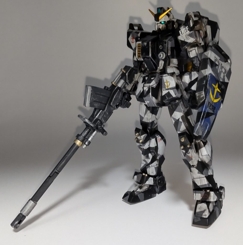 素立ち状態白色と盾の青色は成形色を使っています。マスキングテープをいろいろな形に切り、灰色→黒と塗り重ねていく工程は地味ながら楽しい作業でした。ウェザリングで誤魔化したつもりですが、付属のマーキングシールがやはり浮いて見えますね。でもこのフォントの数字がないとしっくりこない。次はデカールも自作してみようかな？あと塗装後に知ったんですけど、スプリッター迷彩って主に高機動な戦闘機に使われるんですね。都市迷彩の一種か、もしくはこの陸ガンは高速戦闘もいけると自分の中では納得させました。