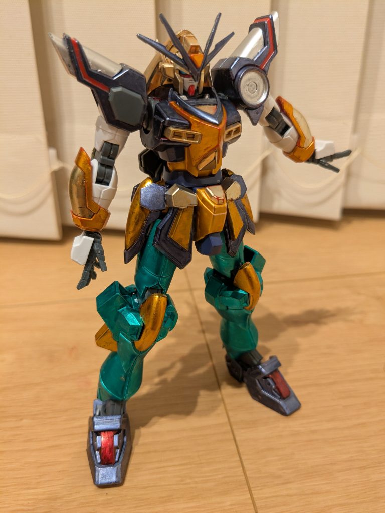 まずは素立ちで1枚。頭は隠岐奈の髪をイメージしてイエローゴールドに、冠をイメージしてアンテナをメタリックダークブルー、アンテナ中央をメタリックオレンジです。体は狩衣イメージで、中央をメタリックオレンジ、ポイントになる部分をイエローゴールド、周辺部をメタリックダークブルーにしました。肩は狩衣の縁イメージでメタリックダークブルー、エフェクト部分は装束に見立ててシャインシルバーで、左肩の〇部分は、彼女の持つ鼓をイメージしてシャインシルバーにしてみました。腕も狩衣と装束に合わせて、白は成型色で、装甲をメタリックオレンジとイエローゴールドで塗装。脚はパンツスカートみたいなイメージがあったので、メタリックグリーンでエフェクトをメタリックオレンジ、足はブーツのイメージでメタリックダークブルーに、靴紐に見立ててロイヤルメタレッドです。