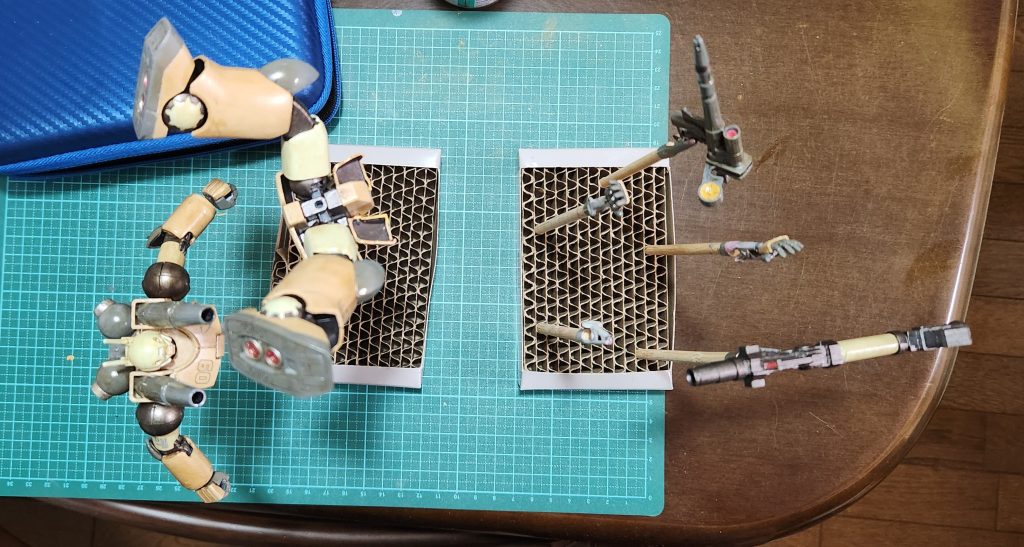 ウェザリング(1回目)+デカール貼り後のつや消し乾燥待ちの様子。リアルタッチマーカーの茶色にてスミ入れ兼ウェザリング1回目やりました。ついでにデカール貼りも。左脛の09の0上部が欠けたのと(アシタのデカールのフィルム剥がしで)右腕に貼った連邦のロゴがつや消しスプレー中に吹っ飛びました(n敗)。