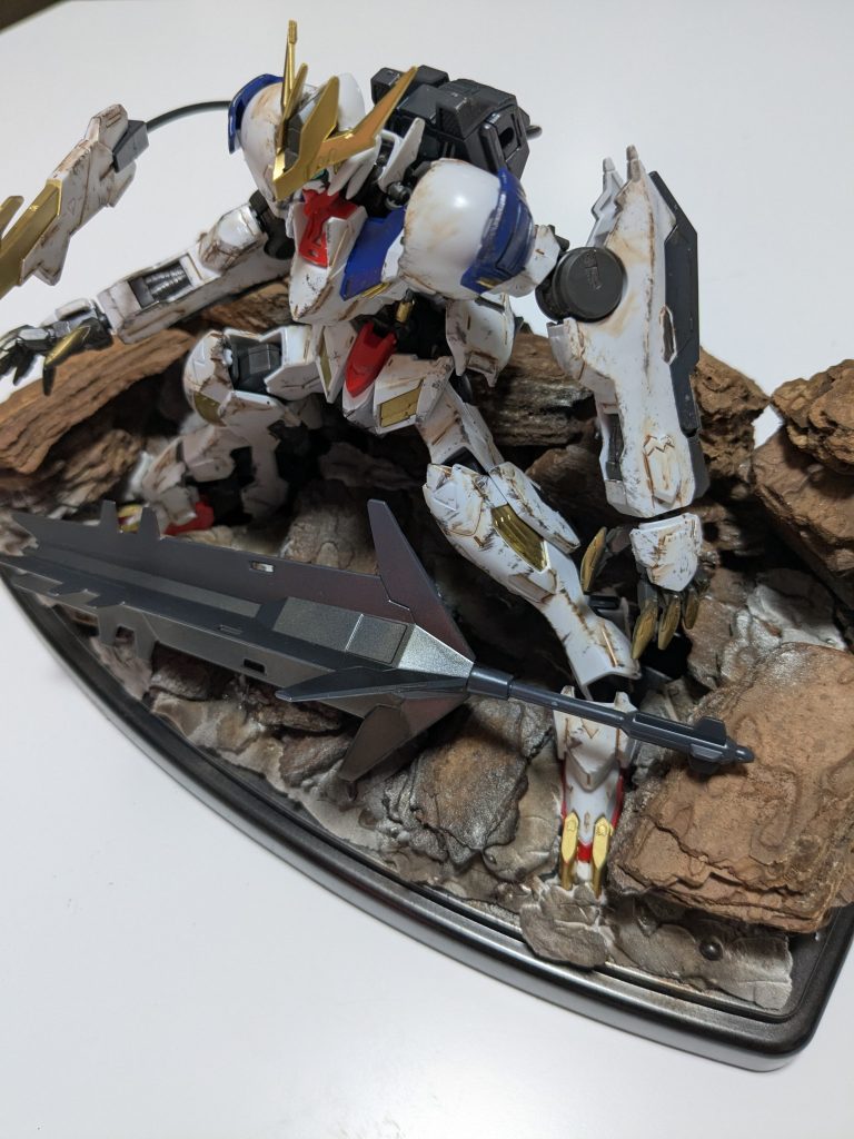 で、更にジオラマっぽくしたくなり、…ただ、そんなにお金もかけられないこのご時世なので、100均でケースと紙粘土、観葉植物用の何かよく分からない木の欠片を購入して、作ってみました。GUNSTAで投稿出来るレベルでは無いのは承知の上で投稿します。何かと初めての事にチャレンジして、正直、面白いと感じたのでまた次回も何かチャレンジしたいと考えてます。あと、バルバトスを組まれて、塗装やジオラマを作られてる方がおられれば、眼光エフェクトのアイデアを頂ければありがたいです。