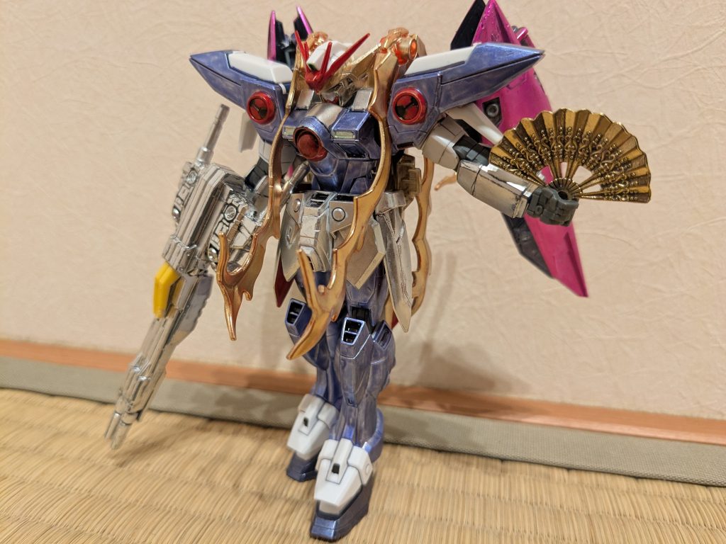 角度を変えて1枚。頭は頭頂部をキャップイメージで成型色のまま、その下は髪をイメージしてイエローゴールド、アンテナはキャップの紐イメージでロイヤルメタレッドです。体や肩はメインにメタリックバイオレット、アクセントにシャインシルバーとロイヤルメタレッド。腕は手袋イメージして、スカートはフリルをイメージしてシャインシルバー。で、脚をどうするか悩んだのですが、最近のイラストでマーメイドドレスみたいな細身のスカートを履いているイメージがあったので、脚もメタリックバイオレット、足首ガードを成型色、スリッパ部分をメタリックダークブルーにしました。で、体と肩の隙間にカミキバーニングの炎エフェクトを挟み込んでイエローゴールドに塗り、紫の束ねた髪に見立ててみました。バスターライフルは両サイドに天狗ガンダム作ったときに余ったバックパックを半分に割り、接着してシャインシルバーで塗装してあります。黄色の部分は塗装しておりません。ここの意味はまた後ほど…。扇子は100均にそれっぽいものがあったので、装備させてみました。