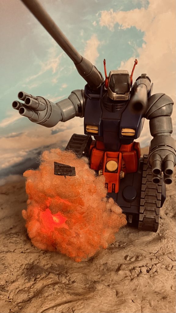 キャタピラに被弾するガンタンクです。右のキャタピラパーツのみを別途メルカリで購入し破損のエフェクトを仕込んでジオラマにしてみました。オレンジのピンポン玉を半分に切り磁石式のLED赤2個を入れて爆発の光を表現しています。手芸用つぶわたで覆いアクリルのオレンジで着色しています。