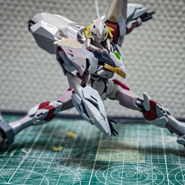 〈設定〉オーブ特別嚮導派遣技術部（通称「特派」）が世界平和機構コンパスと共同開発した試作機動兵器。格闘機であるコンパスのイモータルジャスティスをベースとし、地上での運用を想定した「ランドスピナー」や超振動ロングソード「MVS」、高性能新型センサー「ファクトスフィア」を装備している。ヴォワチュールリミュエールを応用した高機動ユニット「エナジーウィング」が搭載予定である。本機はロールアウト直前の為、1部フェイズシフト装甲の電圧調整がされていない。未完成である。（1枚目）