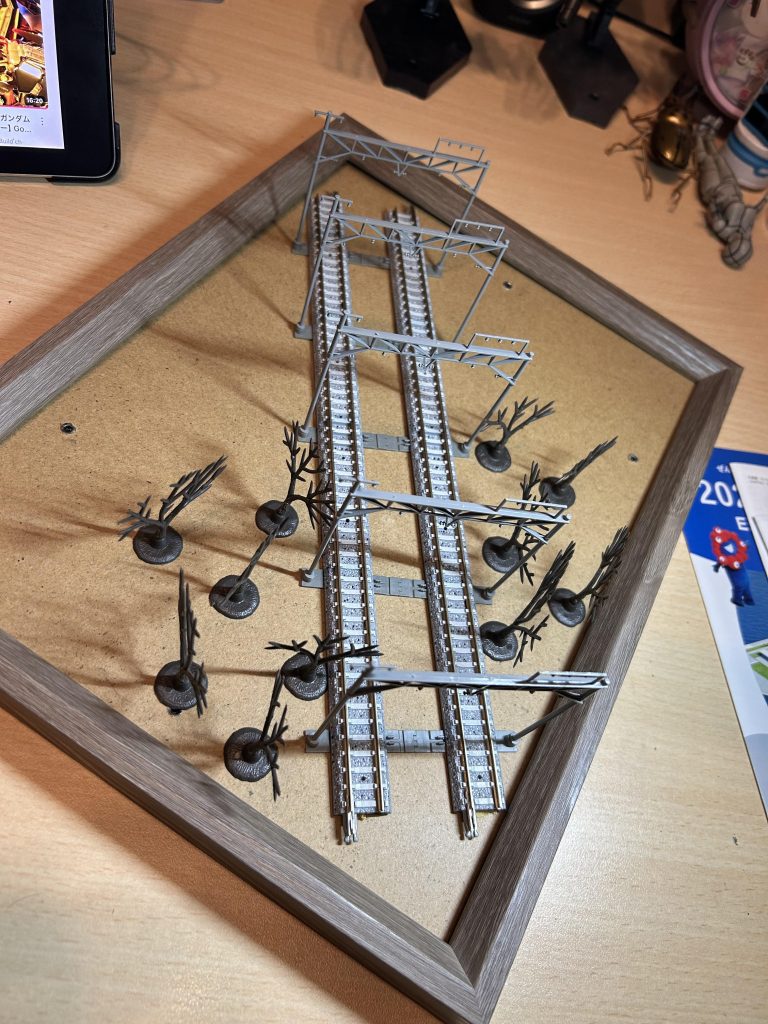 ジオラマは百均のフォトフレームにNゲージのアイテムを配置して、紙粘土に埋め込んで塗装。下手すぎて紙粘土に毎日ちょっぴりヒビが入るので毎日毎日綿棒にペーストをつけて誤魔化しています。