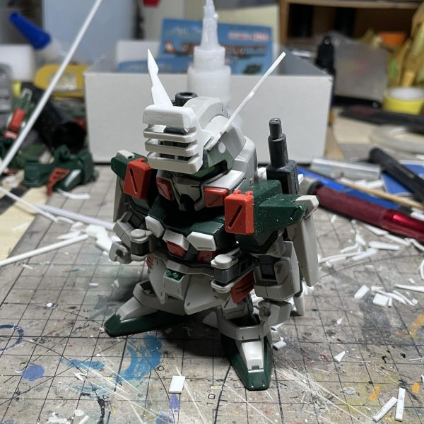 一年前、SDヴェルデバスターガンダムをベースにSDバスターガンダムへ改造した際の工程記録を公開します。最終章は「頭部」の改造工程です。【頭部改造】1. アンテナの制作 設定資料を基にアンテナ形状を確定し、プラ板で作り、そして頭部緑パーツに矩形スロットを切削し、アンテナを埋め込み  2. 可動式防弾装甲取り外し後の処理可動式防弾装甲取り外しで、露出した緑パーツの円孔をプラ棒で埋め戻し3. バスターガンダム特有のセンサー防弾装甲再現    設定画を参照し防弾装甲の造型をSD頭部サイズに最適化（幅調整）、そしてプラ板で制作。  4. 頭部改造完成  センサー防弾装甲を組み込み、頭部の変換を完了【完結】  これをもって、SDヴェルデバスターガンダムからSDバスターガンダムへの改造は全て完了いたしました！ （7枚目）